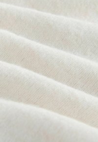 White fabric with a textured, knitted appearance, featuring soft, fine strands and faint variations in shade across the surface.