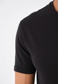 Schwarzes Kurzarm-T-Shirt mit glatter Textur und Rundhalsausschnitt. Verfügt über sauber verarbeitete Nähte und eine taillierte Silhouette.