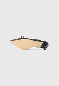 Black high-heeled shoe with a pointed toe, textured upper, and a beige sole. Features a small loop accent at the heel.