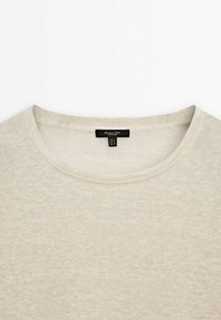 T-shirt corto beige chiaro a maniche corte realizzato in tessuto morbido, con collo rotondo e un'etichetta con informazioni sulla taglia cucita all'interno.