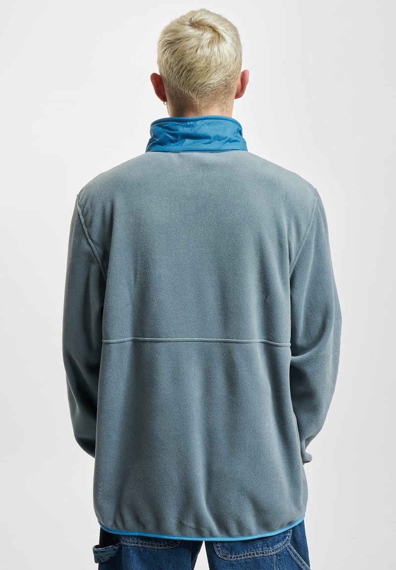 Pullover in fleece grigio con colletto blu, presenta un design senza cuciture e maniche lunghe, mostrando una texture morbida e una vestibilità rilassata.