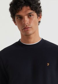 Donkerblauwe gemêleerde trui met een ribbelkraag. Bevat een klein oranje logo op de linkerborst. Casual pasvorm, minimalistisch ontwerp.