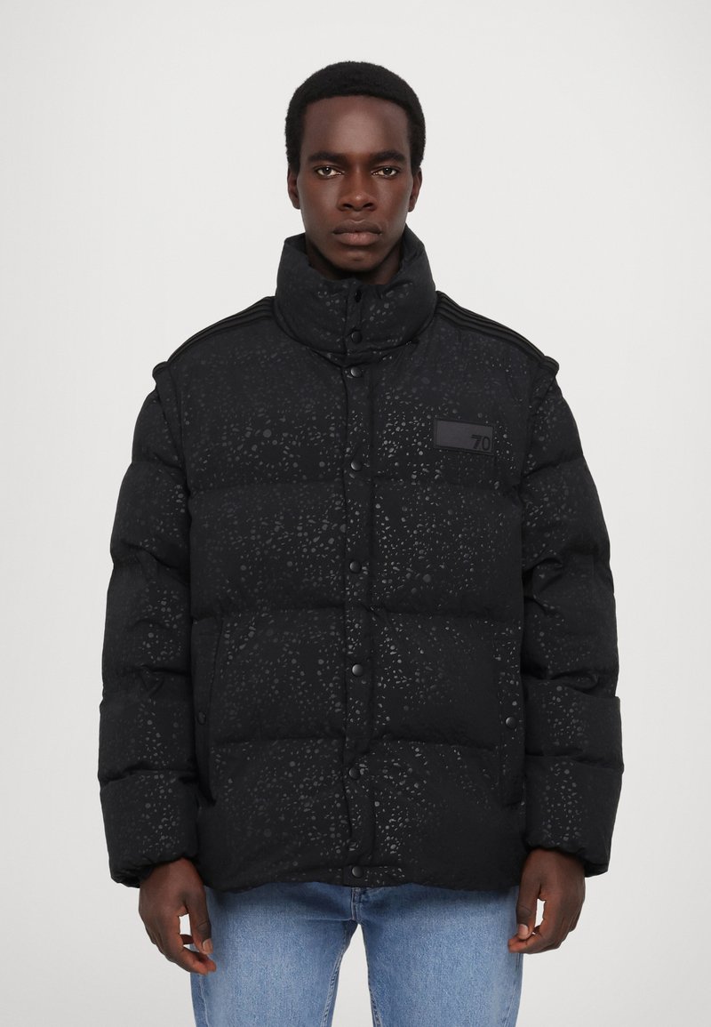 Czarna kurtka puchowa z teksturowanym wzorem, wysokim kołnierzem, zatrzaskami i detalem z naszywką. Posiada wypełnione sekcje oraz luźny krój.