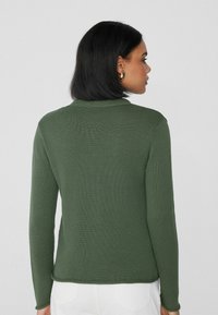 Jersey de color verde oscuro con relieve, de mangas largas, cuello redondo y silueta ajustada, que presenta una textura suave y un dobladillo cuidado.
