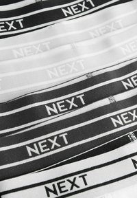 Des élastiques noirs et blancs présentent le mot "NEXT" dans un texte contrasté, disposé en couleurs et motifs alternés. Texture lisse.