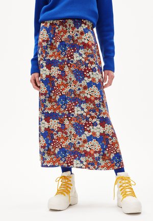 Blomstret midi-nederdel med tætte røde, blå og hvide blomster, båret med blå sweater, blå strømpebukser og hvide støvler med gule snørebånd.