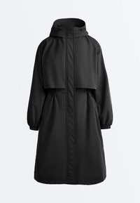 Parka longue noire à capuche avec poignets élastiques, fermeture éclair avant recouverte d'un rabat coupe-vent et une cape superposée sur les épaules.