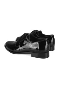 Une paire de chaussures de ville en cuir noir brillant avec des lacets, des talons bas et des bouts arrondis lisses, présentée à un angle diagonal arrière sur fond blanc.
