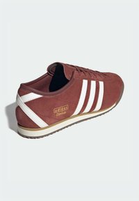 Κόκκινο-βουργουνδί αθλητικό παπούτσι από σουέτ με λευκές τρεις ρίγες και λεπτομέρειες. Διαθέτει χαμηλό προφίλ, σχέδιο με κορδόνια και υφασμένο καουτσούκ στη σόλα.