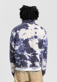 Fleece pullover in navy and cream with a cloud-like pattern. High collar, relaxed fit, with a textured, soft surface.