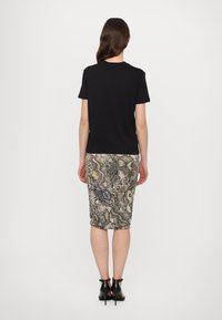 Chemise noire à manches courtes associée à une jupe crayon ajustée à motif serpent dans des tons terreux, complétée par des talons à lanières noirs.