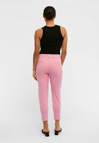 Pantalon rose à coupe fuselée et taille élastique. Tissu lisse et poches arrières. Associé à un haut sans manches noir.