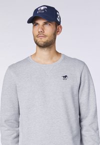 Grauer Sweatshirt mit gesticktem Logo auf der Brust und dunkelblauem Cap mit Logo und der Zahl "3" an der Seite, beides lässig und bequem.