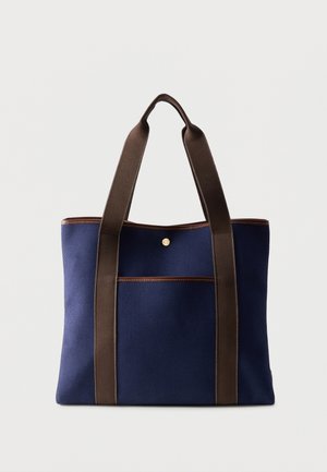 Τσάντα χειρός από καμβά σε ναυτικό μπλε με σκούρες καφέ λαβές και διακόσμηση, με μπροστινή τσέπη και μία κούμπωμα με πατούρα.