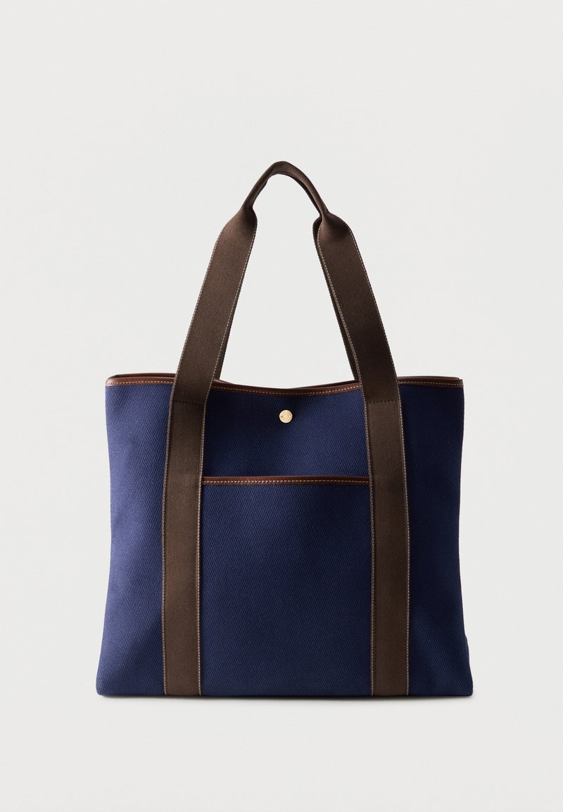 Τσάντα χειρός από καμβά σε ναυτικό μπλε με σκούρες καφέ λαβές και διακόσμηση, με μπροστινή τσέπη και μία κούμπωμα με πατούρα.