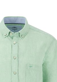 Camicia di lino verde chiaro con colletto button-down, patta frontale e taschino sul petto con un logo ad albero discreto.