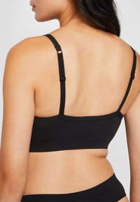 Svart bomulls-bralette med justerbara remmar och bred kant. Har en mjuk textur och minimala sömmar för komfort.