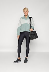 Chaqueta ligera a dos tonos en verde menta y gris claro, combinada con leggings negros y zapatillas negras, llevando un bolso negro.