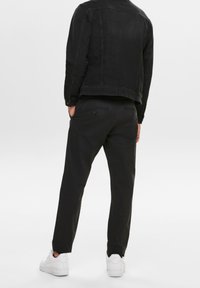 Giacca di jeans nera abbinata a pantaloni neri. Entrambi hanno un design semplice. Sneakers bianche con suole testurizzate completano l'outfit.