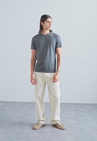 Grå t-skjorte med korte ermer, hvite vide bukser og beige sneakers. Glatt stoff, avslappet passform og enkelt design. Ingen synlige mønstre.
