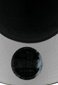 Schwarzstoffmütze mit grauem Schirm, versehen mit einem runden Etikett mit "9FORTY M-CROWN" und "NEW ERA"-Text in glänzender Optik. Verstellbares A-Frame-Design.