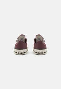 Burgundia suede Converse All Star kingad, madala lõikega disain, beež kummist talla ja iseloomuliku brändingu tõstepinnal.