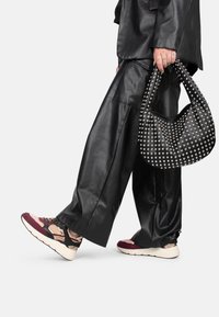 Black faux leather oversized pants paired with patterned sneakers in burgundy, black, and beige. A studded black handbag completes the look.