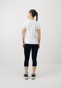 T-shirt blanc à manches courtes associé à un legging capri ajusté bleu marine et des baskets noires avec des accents néon, vu de dos.