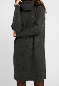 Abito maglione grigio a maglia con collo alto a sciarpa, maniche lunghe, texture a coste e vestibilità comoda che arriva a metà coscia.