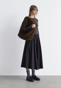 Brown long-sleeve top, black pleated skirt, gray socks, and black shoes. Model holds a brown faux-fur bag. Simple, modern design.