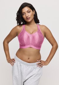 Reggiseno sportivo rosa con motivo geometrico a rilievo, spalline regolabili e fascia solida. Abbinato a pantaloni della tuta grigi.