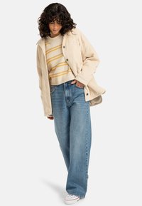 Beige corduroy jacket, yellow-striped sweater, loose blue jeans, and white sneakers; flat design with buttons and pockets.