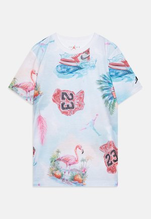 T-shirt in cotone con una base bianca e stampe tropicali colorate, che includono fenicotteri, elementi di basket e sneakers in tonalità vivaci.