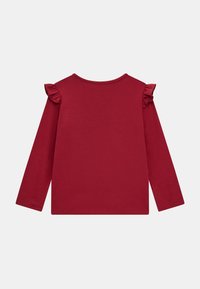 Top a maniche lunghe di color bordeaux realizzato in un tessuto morbido, con dettagli arricciati sulle cuciture delle spalle. Design semplice con scollatura a girocollo senza dettagli frontali.