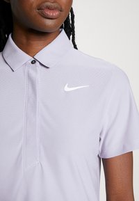 Fialová polo košile s límečkem, krátkými rukávy a bílým logem Nike na levé části hrudi. Texturovaná tkanina s hladkým povrchem.