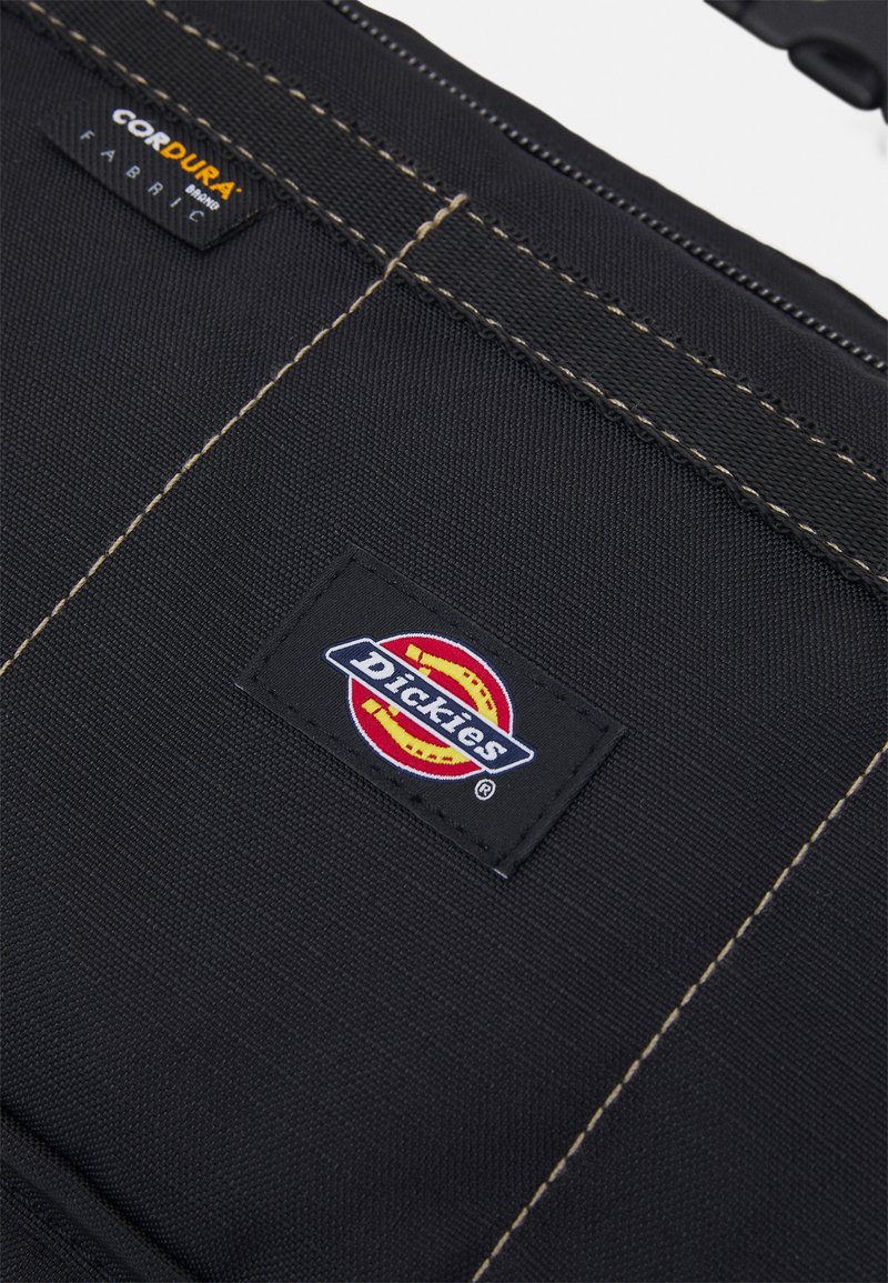 Tessuto Cordura nero con cuciture gialle e una patch rettangolare del logo Dickies con elementi rossi, gialli e blu.