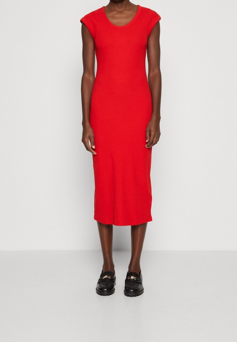 Robe midi rouge sans manches avec encolure dégagée, en tissu extensible, silhouette ajustée et texture lisse. Personne portant des chaussures noires.