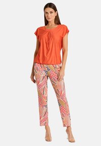 Rotes kurzärmliges Oberteil mit gerafftem Detail am Halsausschnitt, kombiniert mit einer gemusterten Hose mit abstrakten Blumenmotiven in Pink und Orange.