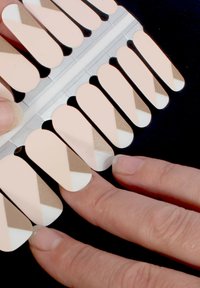 Nagelwickel zeigen ein geometrisches Design mit beigen, weißen und goldenen Akzenten auf einem hellrosa Grund. Die Textur wirkt glänzend und glatt.