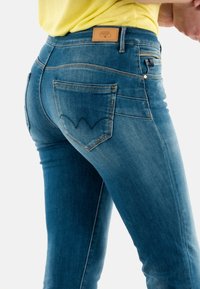 Jeans in denim blu con un design aderente, caratterizzati da tasche posteriori e un motivo a onde distintivo cucito. Fodera in pelle con marchio alla vita.