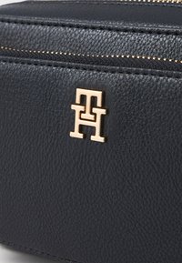 Μαύρη δερμάτινη τσάντα με υφή, με χρυσό ανάγλυφο λογότυπο. Το φερμουάρ περιβάλλεται από χρυσές ραφές, προσδίδοντας αντίθεση και λεπτομέρεια.