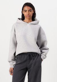 Felpa grigia chiaro con vestibilità rilassata, cappuccio con cordini e polsini a coste. Abbinata a pantaloni felpati grigi scuri, con un design semplice.