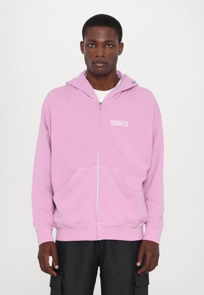 Light pink zip-up hoodie with a front pocket and white logo on chest. Features a drawstring hood and ribbed cuffs and hem.