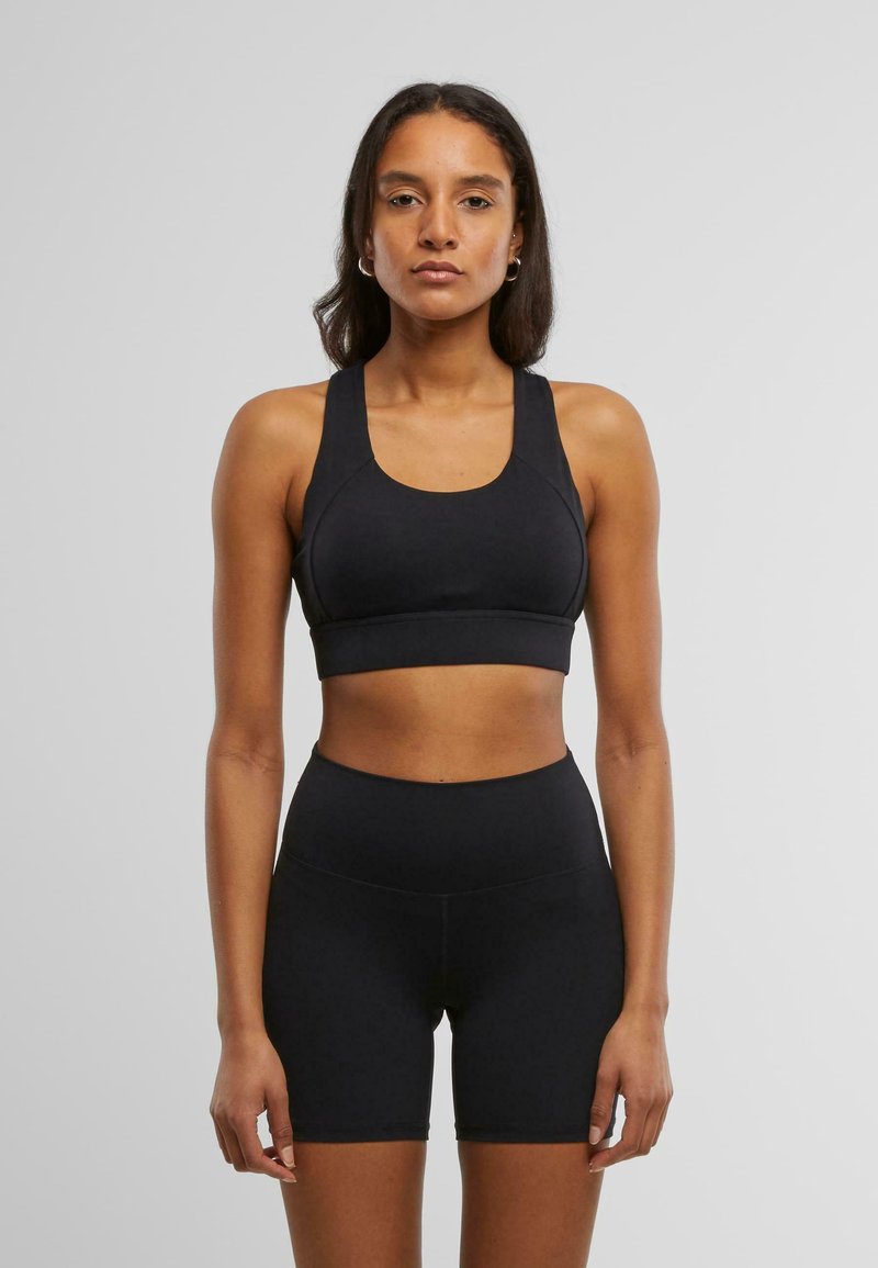 Svart sports bh med brede stropper og rund hals, kombinert med høyt både svarte shorts. Glatt, stretchy stoff med en tettsittende design.