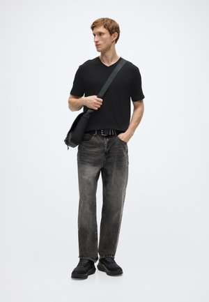 Svart v-hals t-skjorte, falmede grå jeans og svarte joggesko. Har også en svart skulderveske og et teksturert belte. Modellen står sideveis.