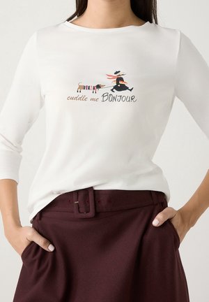 Hvid langærmet skjorte med illustration af en person, der går tur med en gravhund, og teksten "cuddle me BONJOUR" på forsiden.