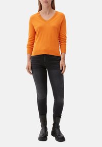 Orangemelerad V-ringad stickad tröja med långa ärmar, kombinerad med svarta skinny jeans och svarta ankelboots. Slät textur och figurnära design.