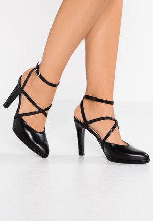 Czarne szpilki o gładkim lakierowanym wykończeniu, z krzyżującymi się paskami na kostce i szpiczastym noskiem.