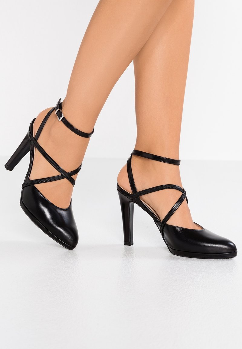 Chaussures à talons hauts noires avec une finition brillante élégante, dotées de brides autour de la cheville en croix et d'un design à bout pointu.