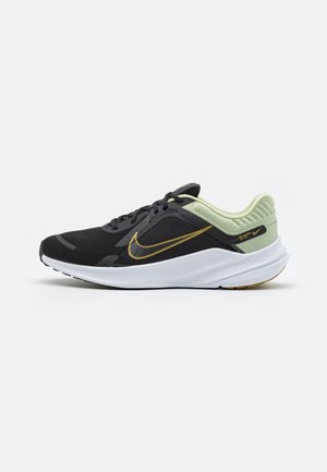 Zapatilla de correr Nike en negro y verde claro con suela blanca y logo dorado, vista lateral sobre fondo claro liso.